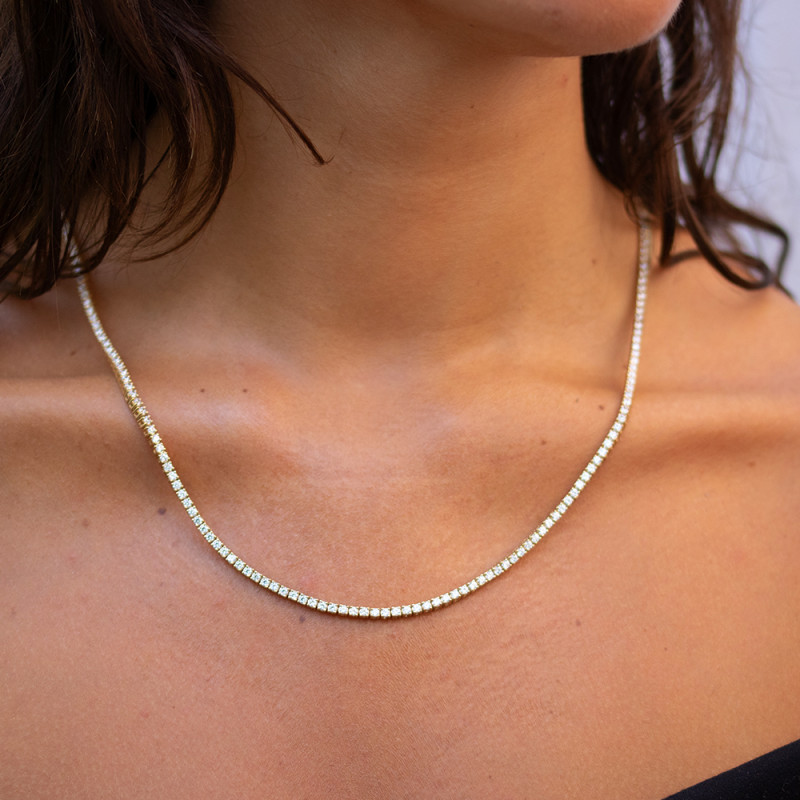 Diamanten rivière ketting in 18 karaat geelgoud, gedragen op een vrouwelijk decolleté — Celinni sieraad met warme uitstraling en continue schittering