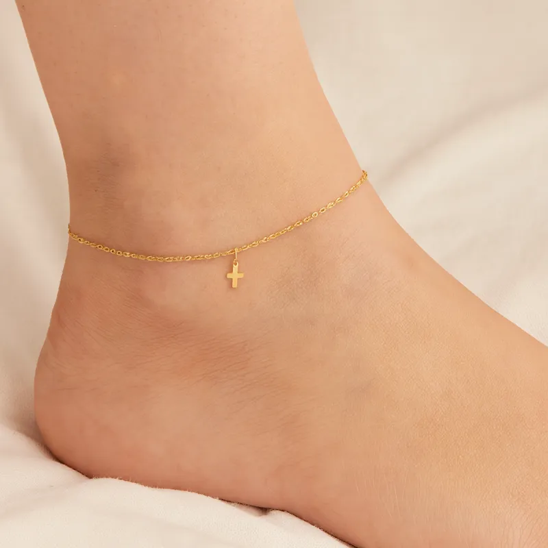 Delicate yellow gold anklet featuring a small cross pendant, worn elegantly around the ankle