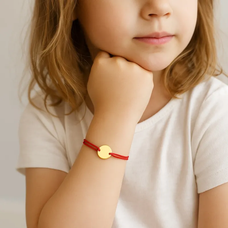 Bracelet en cordon rouge avec médaille ronde en or, représentant le symbole du fil rouge et la signification d’un lien d’amour ou de protection.