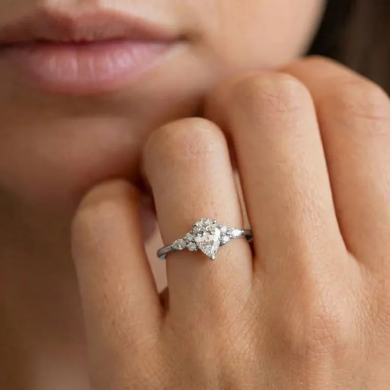 Mano con un anillo de compromiso de diamante talla pera rodeado por un halo de diamantes sobre montura de oro blanco, estilo elegante y sofisticado