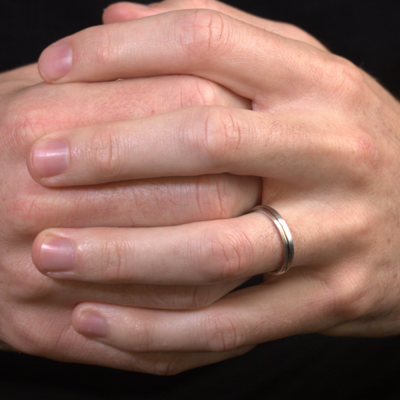 Gros plan sur les mains d’un homme portant une bague en or blanc minimaliste, illustrant l’élégance et la signification d’un bijou pour homme.