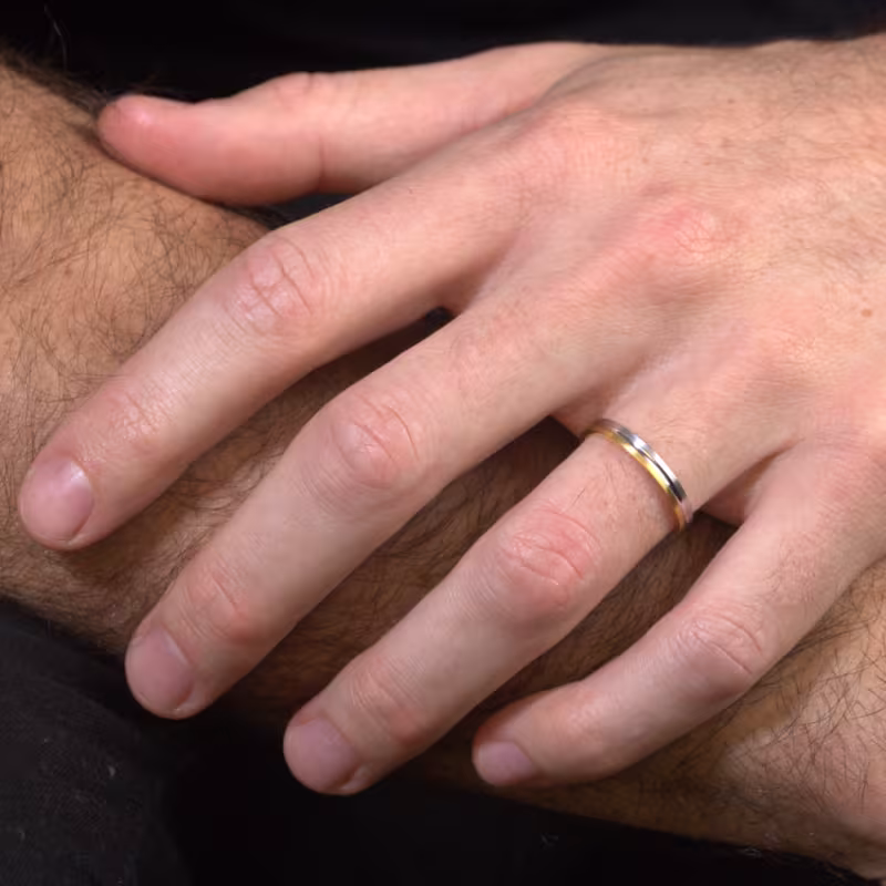 Main d’un homme portant une alliance fine en or, illustrant l’ajustement idéal d’une bague et l’importance de choisir la bonne taille de doigt pour un confort optimal.