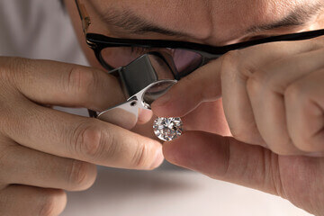 Un gemmologue regarde à la loupe un diamant taille ronde avec un grossissement x10