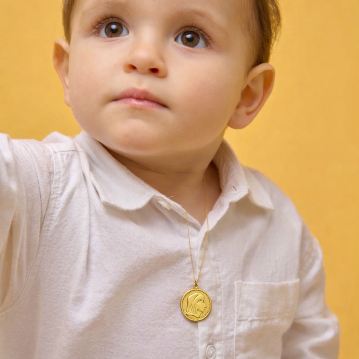 Bébé vêtu de blanc portant une médaille de baptême en or 18 carats, symbole de protection et de transmission lors du baptême