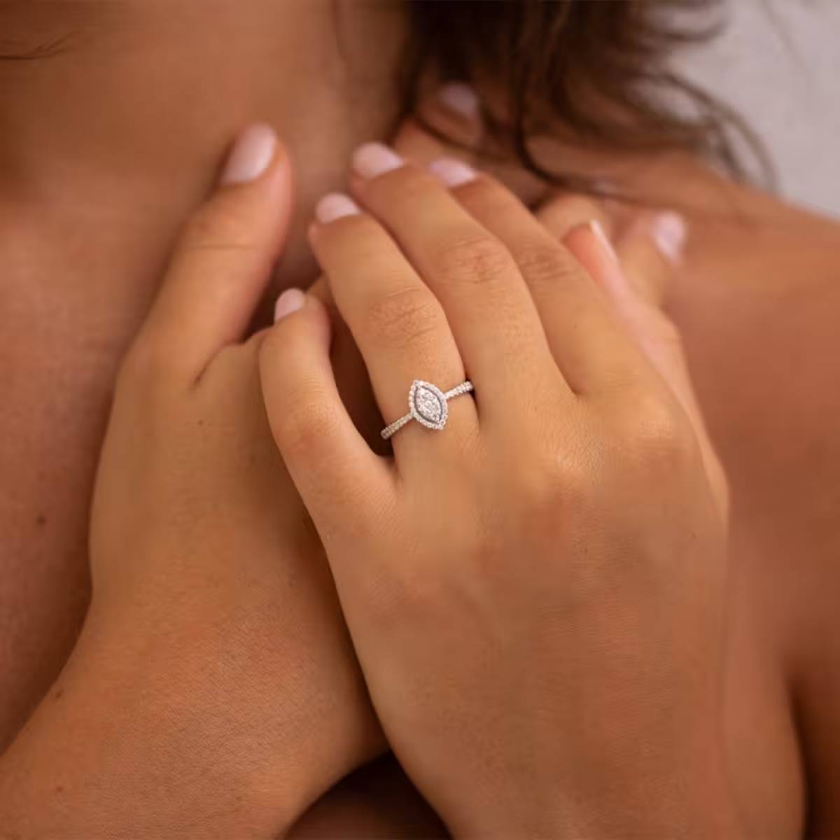 Gros plan sur une main portant une bague de fiançailles marquise en diamant, sertie sur un anneau pavé, création raffinée de la Maison Celinni.