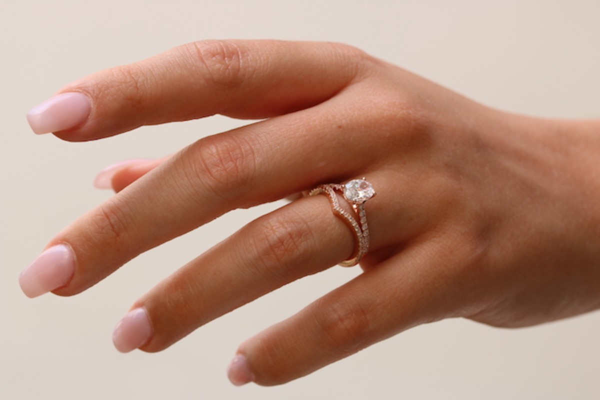 Hand mit einem Verlobungsring aus Roségold mit zentralem Diamanten und pavébesetztem Ring, elegant und raffiniert