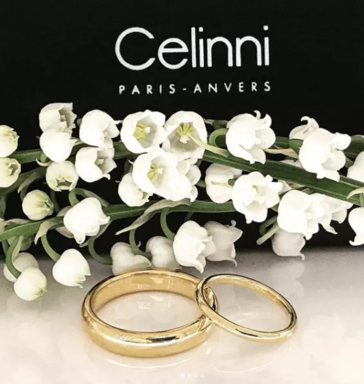 Two yellow gold wedding rings, including one set with sparkling diamonds, displayed with white flowers to showcase elegant ring styles in Lyon.