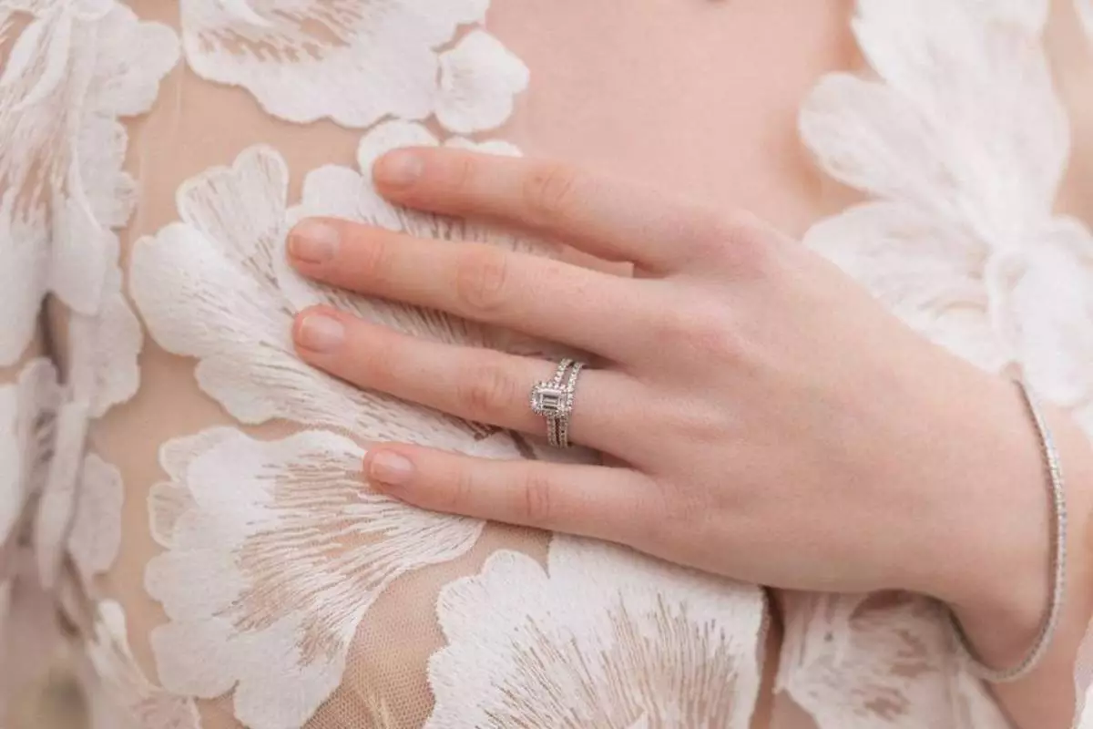 Weibliche Hand mit einem mit Diamanten besetzten Verlobungsring und passendem Ehering, Symbol der modernen Trends 2025.