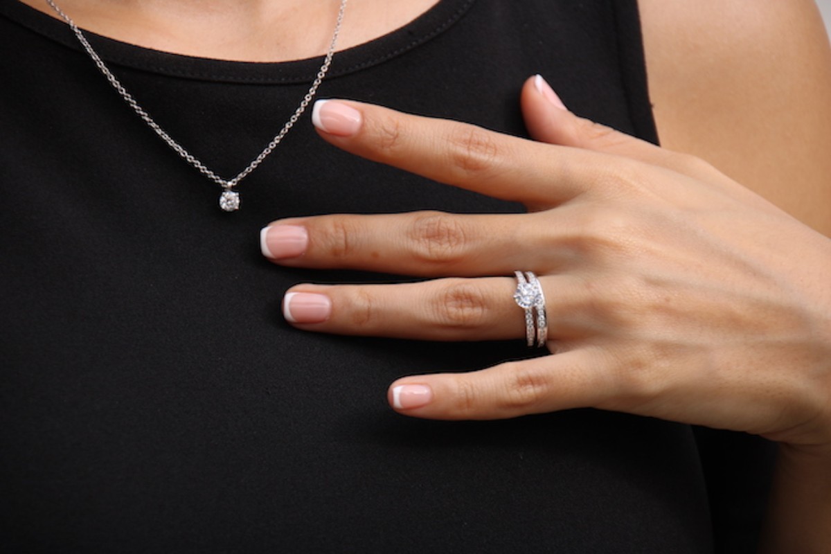 Zoom sur la main d’une femme portant une alliance et une bague en diamant, assorties à un collier élégant. Un bijou raffiné, symbole d’amour éternel, idéal comme cadeau de félicitations de mariage.