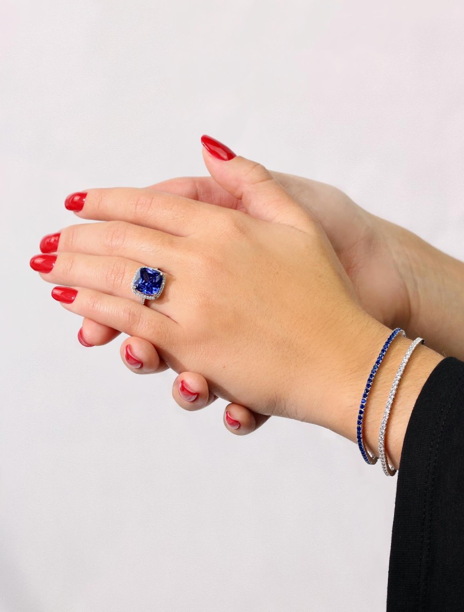 Mano de mujer con anillo de piedra azul tipo zafiro rodeado de diamantes y pulseras finas