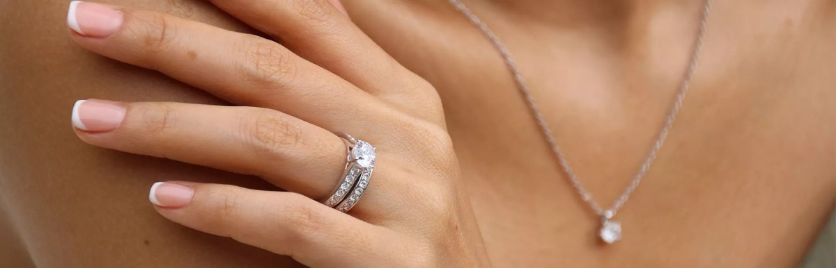 Vrouw die een Celinni solitaire diamanten ring in witgoud draagt met bijpassende trouwring en diamanten hangerketting, symbool van elegantie en toewijding.