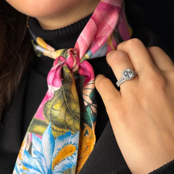 Mano llevando un anillo de diamante halo con una bufanda colorida atada al cuello