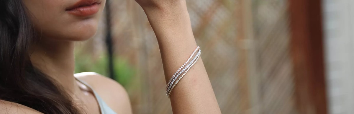 Femme portant trois bracelets en diamants de styles différents, en or blanc, or jaune et or rose, illustrant l’art du stacking joaillier.