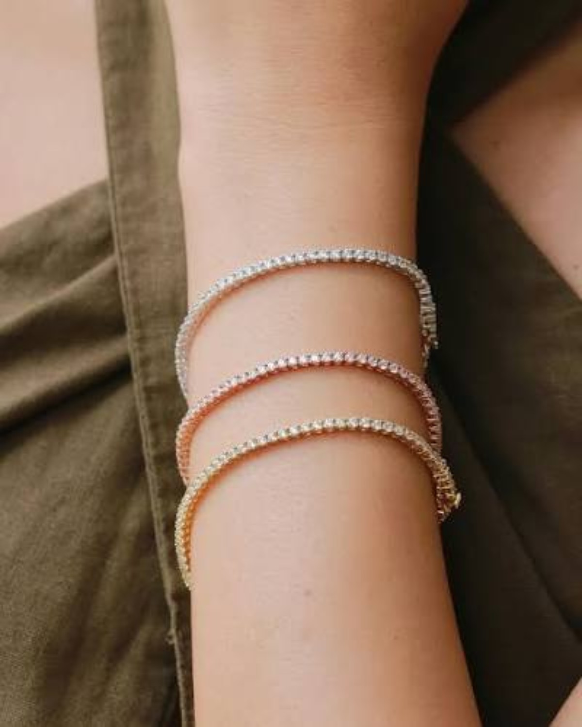 Three delicate natural diamond bracelets in yellow gold, white gold and rose gold worn together on the wrist.
