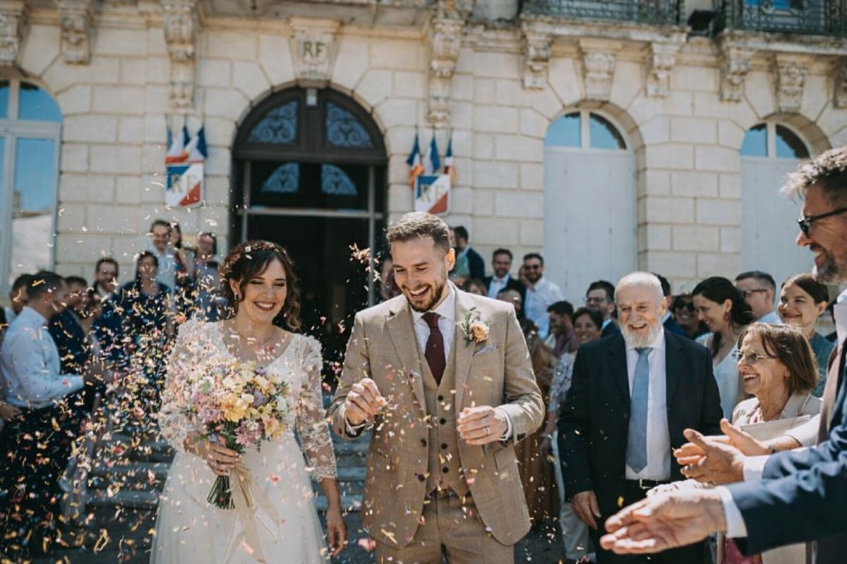 Recién casados saliendo del ayuntamiento tras su matrimonio civil en Francia, recibidos por sus familiares lanzando confeti frente al edificio municipal.