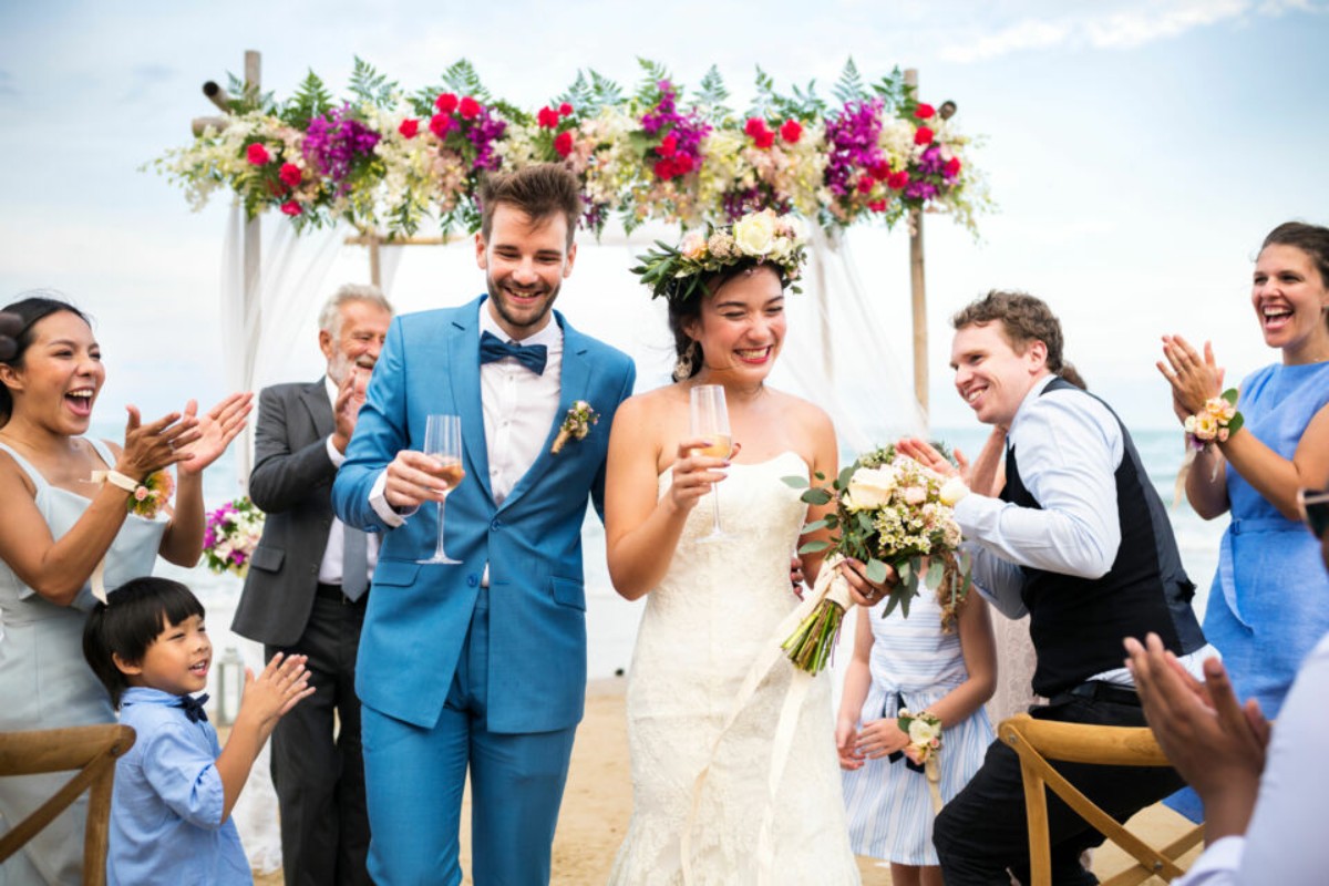 Couple de mariés célébrant leur union sur une plage décorée de fleurs, entouré de leurs proches, symbole de modernité et de joie dans les mariages européens d’aujourd’hui.