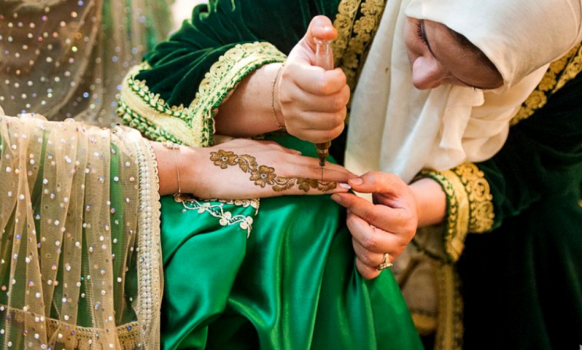  امرأة تضع الحناء على يد عروس ترتدي قفطانًا أخضر، خلال حفل الحناء التقليدي الذي يسبق الزواج في المغرب.