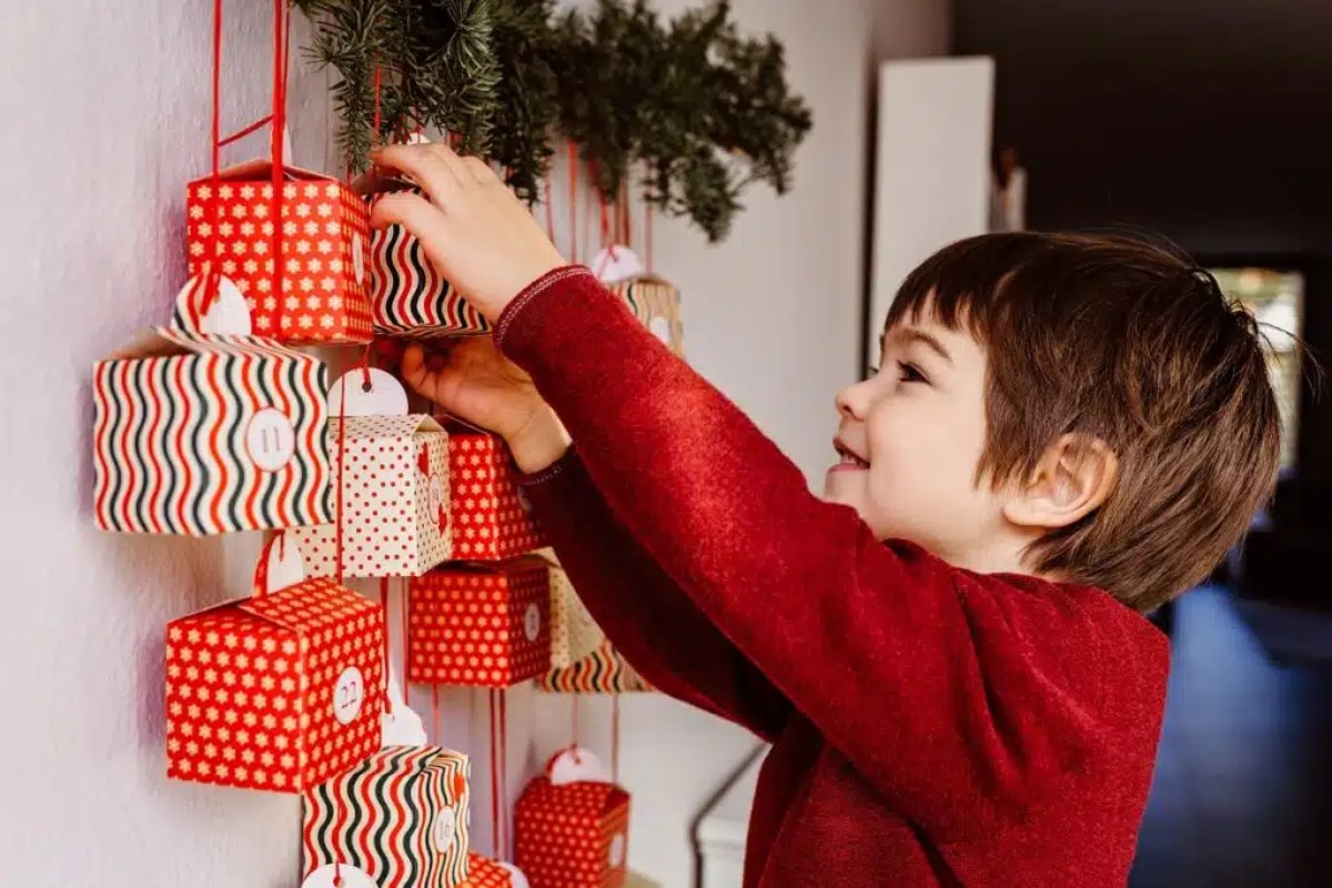 Kind dat een hangende adventskalender opent, versierd met kleine gekleurde doosjes – een weergave van de magie en familietraditie van Kerstmis.