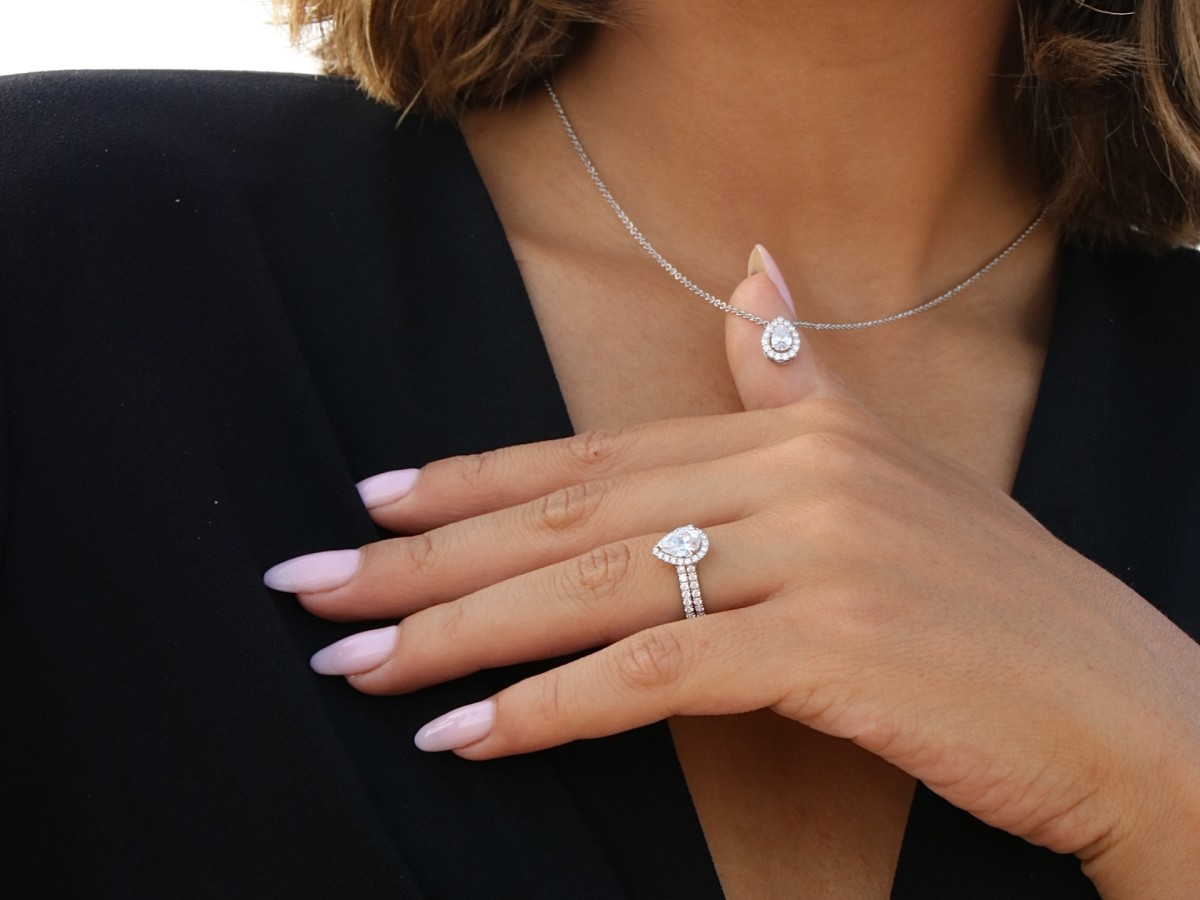 Close-up van een vrouw die een solitaire diamanten collier en een diamanten verlovingsring draagt, symbolen van eeuwige liefde – een prestigieus huwelijkscadeau van Celinni.