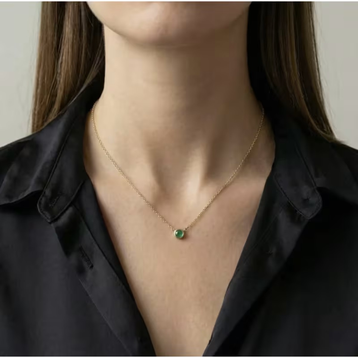 Vrouw die een gouden ketting met groene stenen hanger draagt, voorbeeld van een elegante gouden ketting die regelmatig moet worden gereinigd om haar glans te behouden.