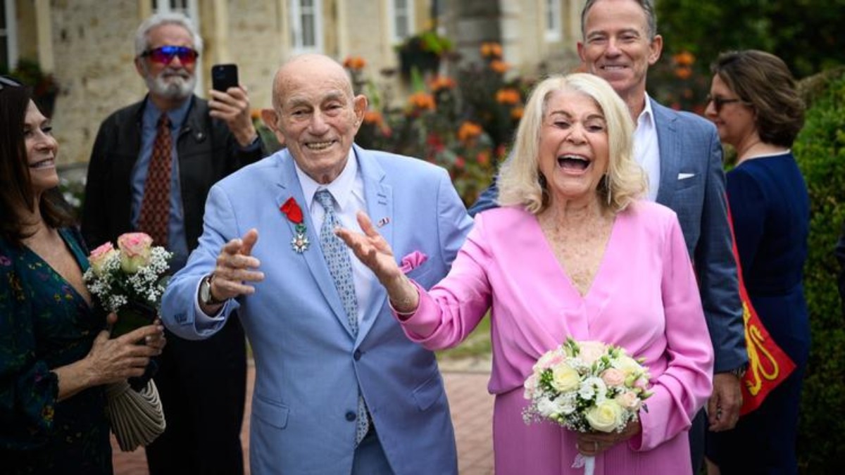 Couple célébrant 100 ans de mariage – Noces d’eau en famille l Celinni Un couple âgé rayonnant célèbre ses noces d’eau entouré de ses proches, bouquet à la main, lors d’une cérémonie pleine de joie et d’émotion.