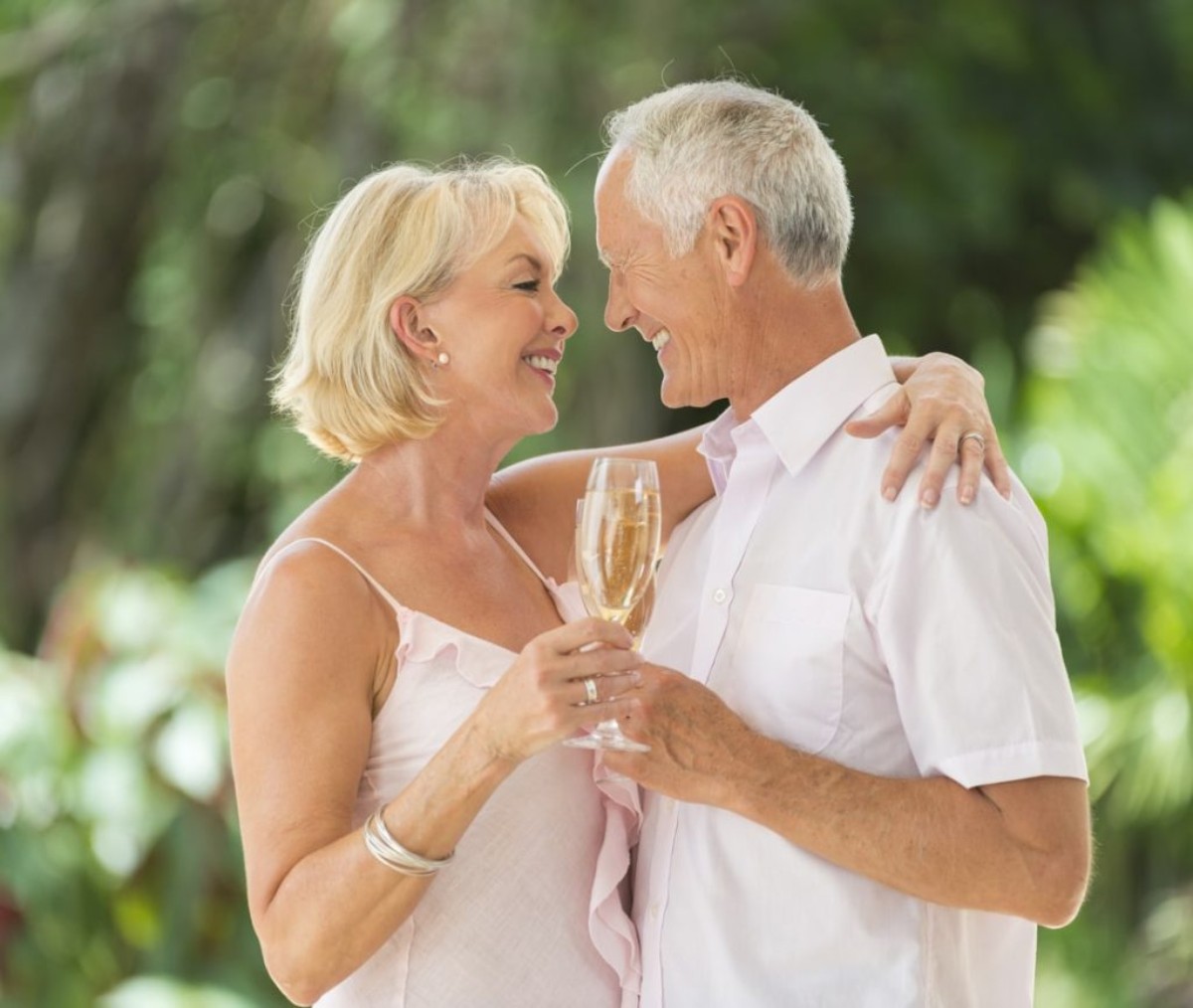 A smiling couple raising a champagne toast in a lush green setting, celebrating their 44 years of marriage and topaz wedding anniversary with joy and emotion.