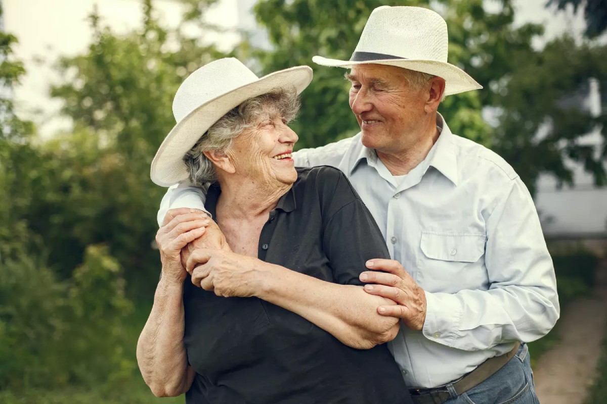 Un couple âgé s’enlace tendrement dans un jardin, symbole d’un amour durable célébré à l’occasion des 55 ans de mariage – noces d’orchidée.