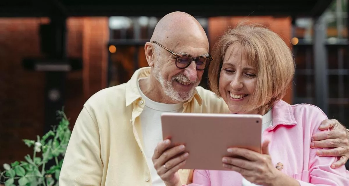Un couple âgé, assis côte à côte, regarde une tablette avec tendresse, revivant les souvenirs de leurs 34 années de mariage à l’occasion de leurs noces d’ambre.