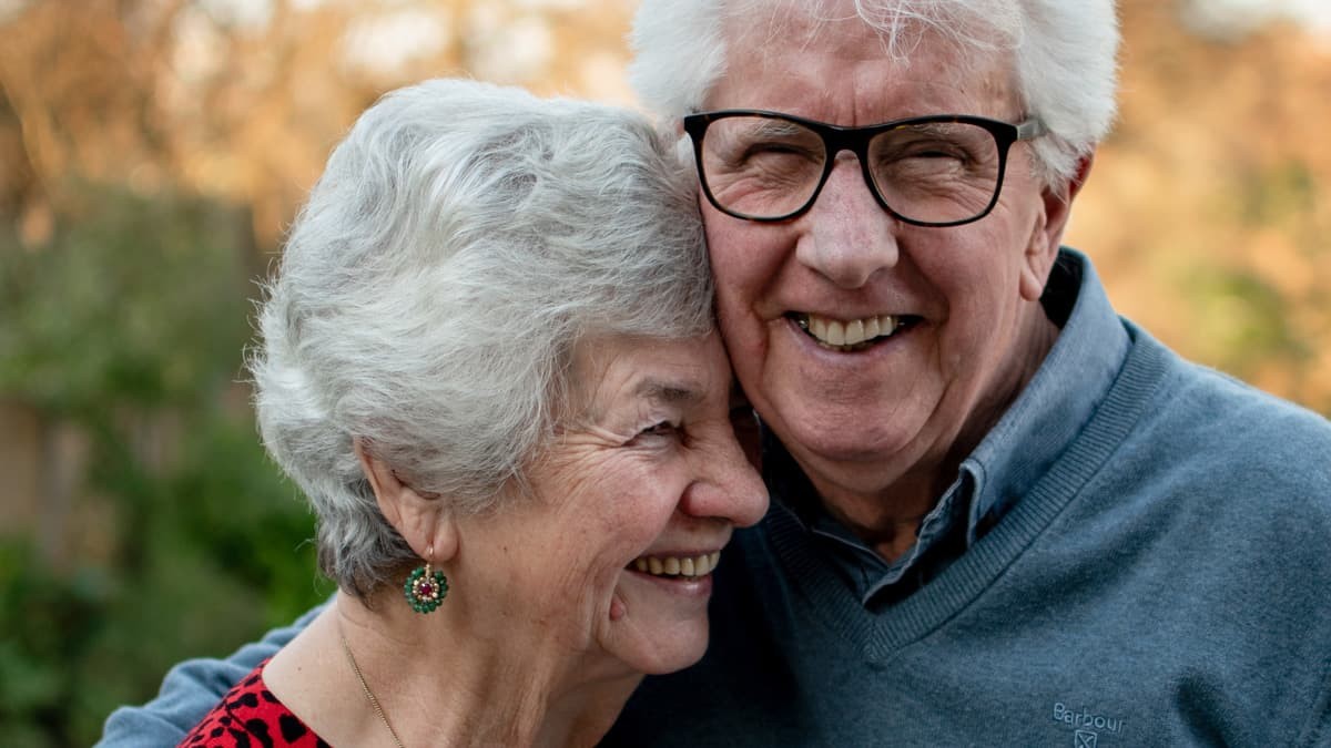 Un couple senior souriant, symbole de complicité et d’amour éternel, fêtant leurs noces d’orchidée après 55 ans de mariage.