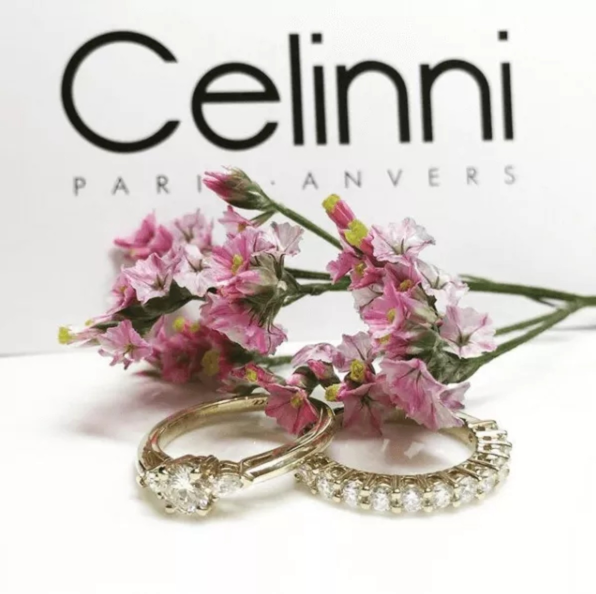 Two wedding rings set with natural diamonds displayed alongside pink flowers, illustrating engagement ring choices at Celinni in Lyon.
