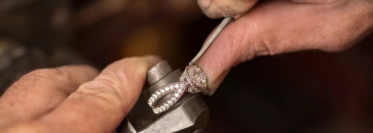 Un artesano joyero de Celinni da forma manualmente a un anillo de compromiso de oro engastado con diamantes, ilustrando el saber hacer personalizado.