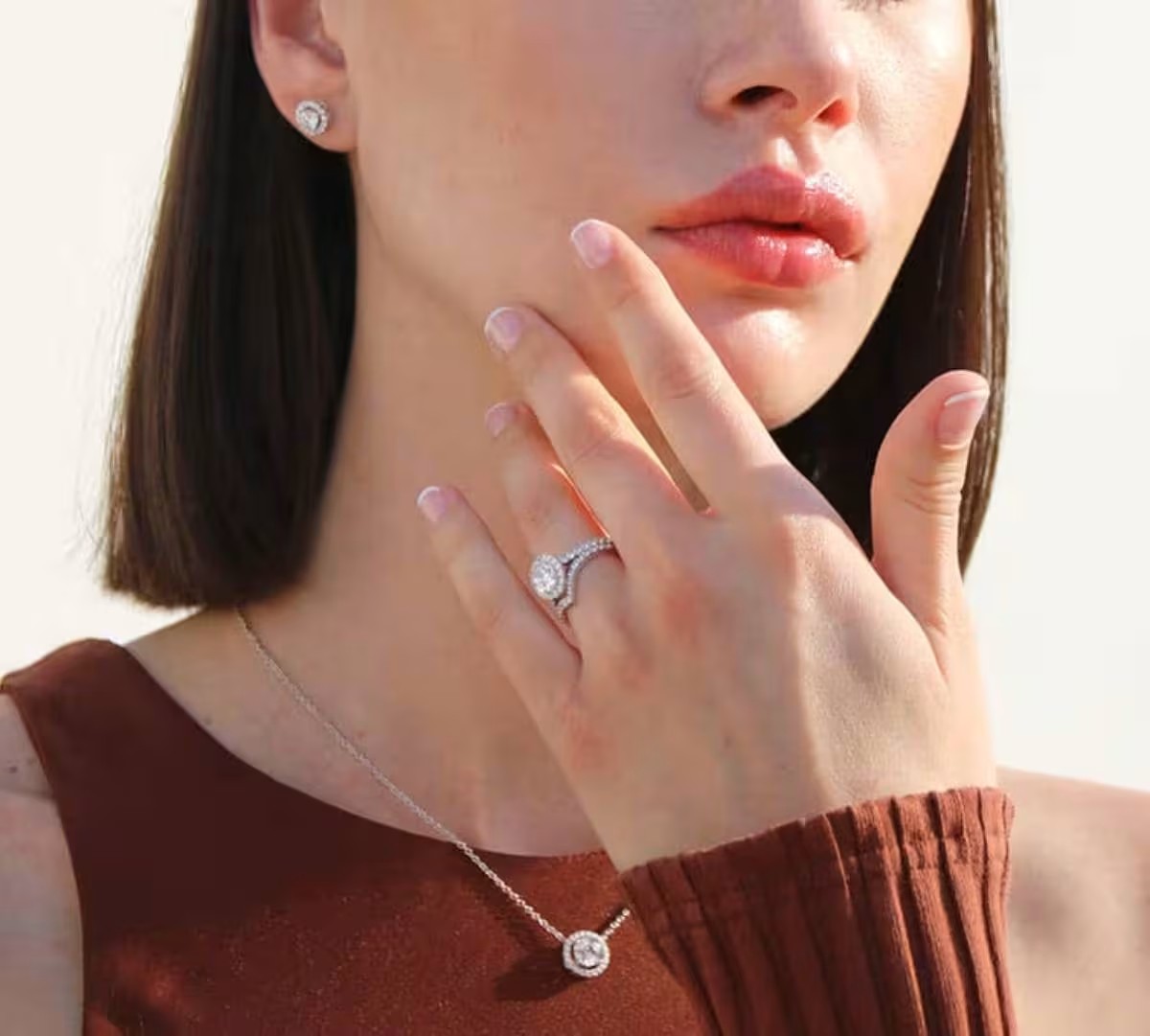 Femme portant une bague de fiançailles serti halo avec alliance pavée, assortie à un collier et des boucles d’oreilles diamant, mise en scène lumineuse Celinni.