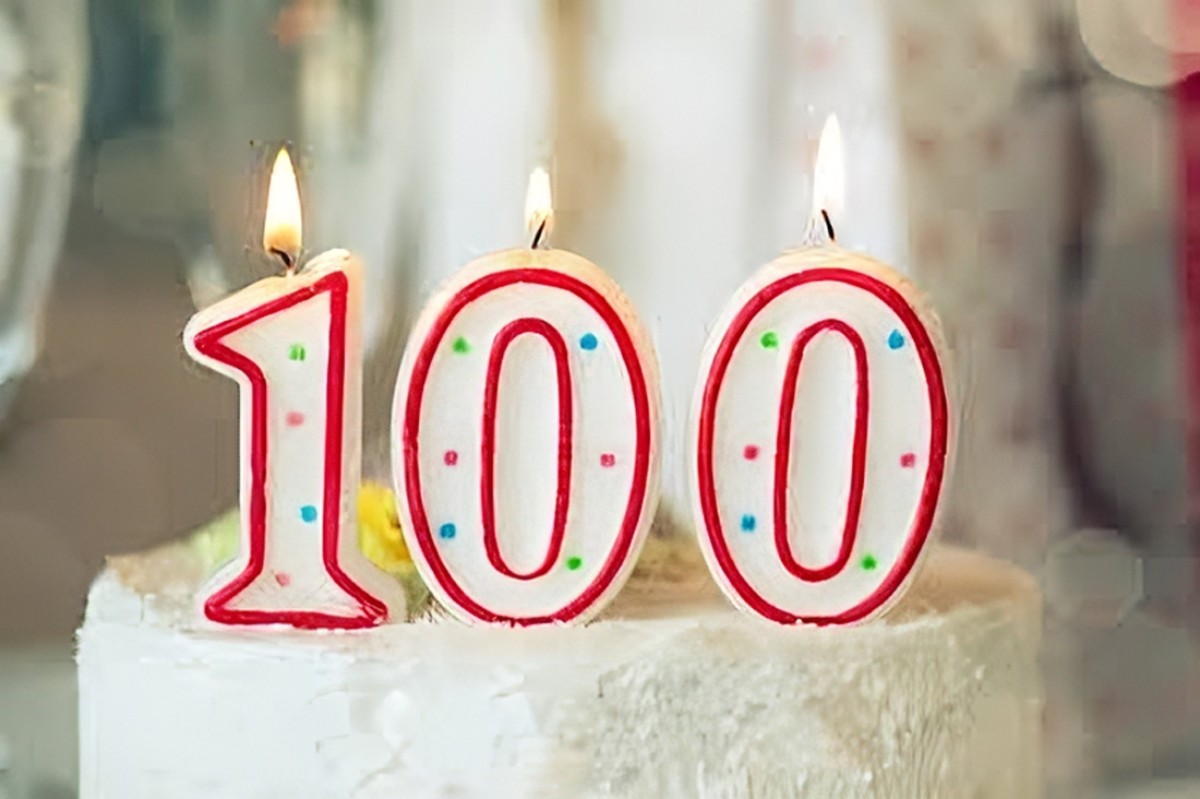 Gâteau d’anniversaire pour 100 ans de mariage – Noces d’eau Gros plan sur un gâteau blanc décoré de bougies en forme du nombre 100, symbole festif des noces d’eau et d’un siècle d’amour partagé.