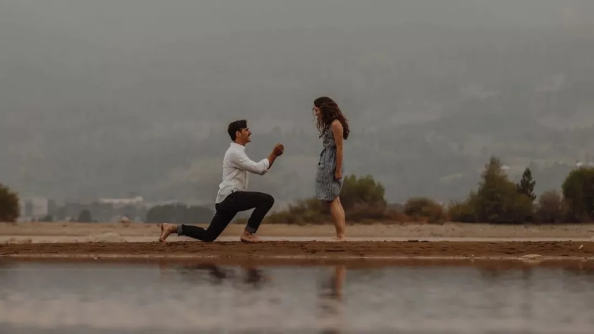 رجل يجثو على ركبة واحدة ويطلب يد شريكته للزواج على الشاطئ عند غروب الشمس