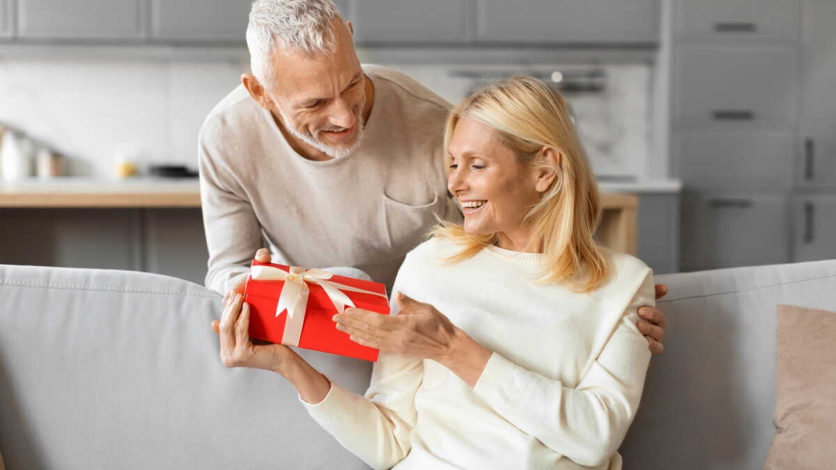 Mari offrant un coffret cadeau à son épouse pour leurs 14 ans de mariage, geste symbolique des noces de plomb célébrant solidité et amour durable.