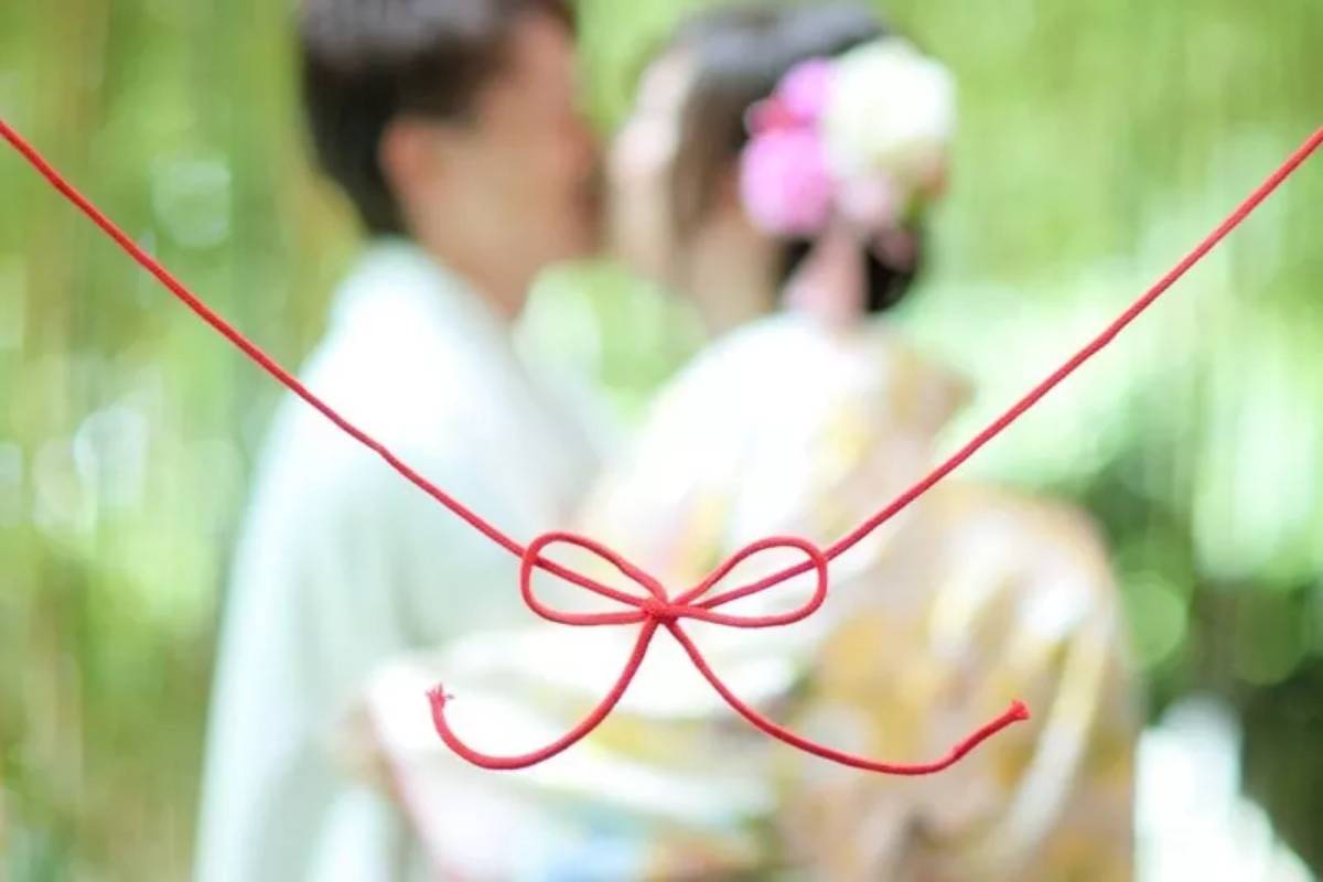 Fil rouge noué en forme de nœud au premier plan, avec un couple flou en arrière-plan, illustrant la légende du fil rouge et l’amour prédestiné.