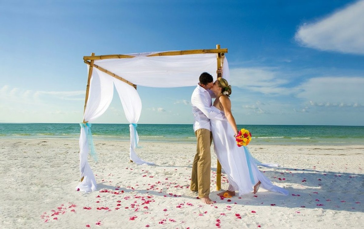 Mariés s’embrassant sous une arche blanche en bord de mer, symbole d’un mariage moderne mêlant liberté, amour éternel et tradition nuptiale européenne.