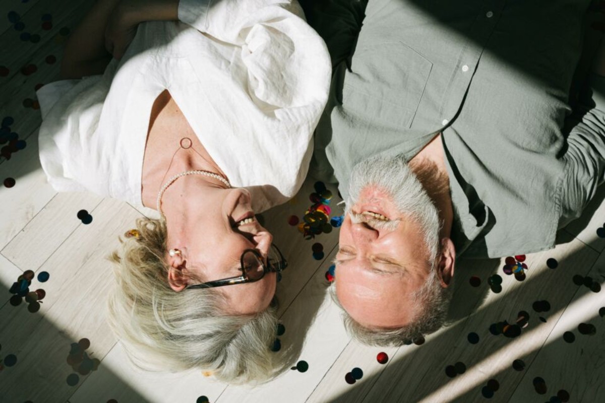 Couple de seniors allongés au sol, souriants et entourés de confettis colorés, célébrant avec bonheur leurs 36 ans de mariage, aussi appelés noces de mousseline.