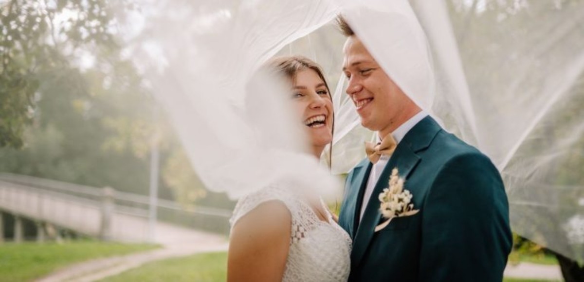 Jeunes mariés souriants sous un voile léger, illustrant la signification des noces de rosée et la délicatesse des premiers mois de mariage.