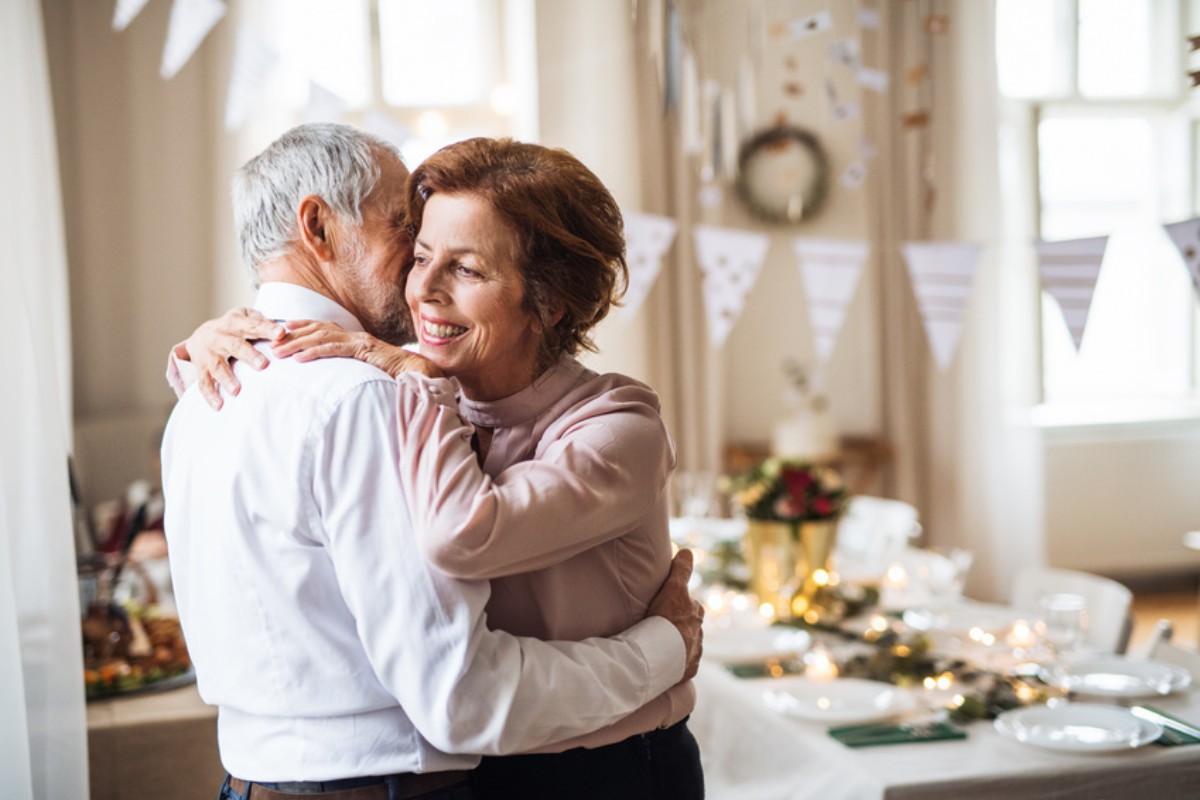 Un couple senior partage un moment de tendresse dans la cuisine, illustrant la complicité quotidienne et l’amour profond qui caractérisent les noces de tourmaline, 52 ans après leur union.