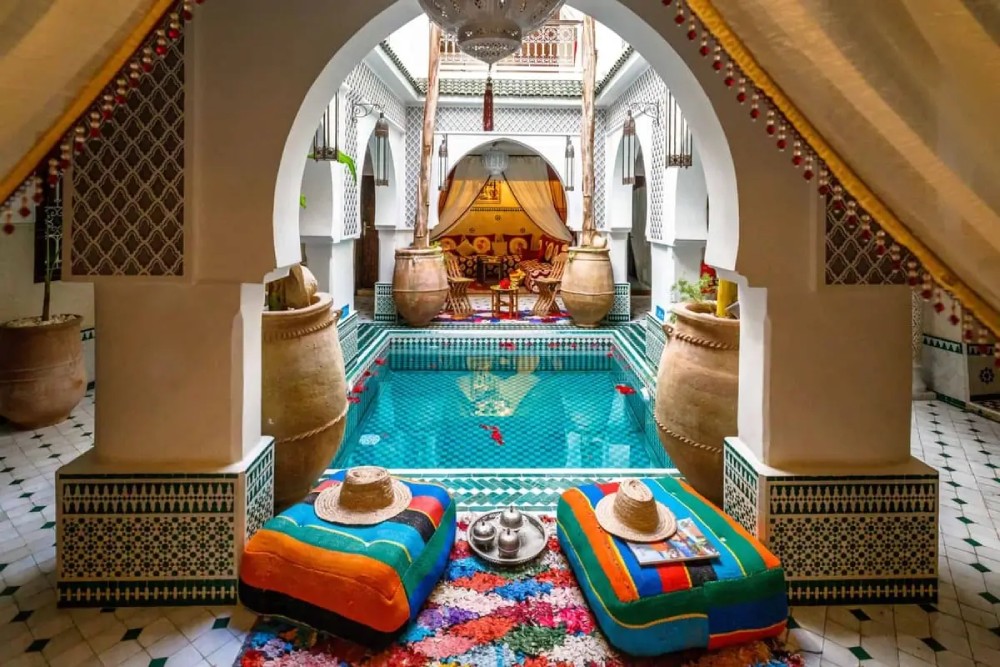 Patio marocain avec piscine turquoise, lanternes et coussins colorés dans un riad traditionnel de Marrakech, idéal pour une demande en mariage intime et authentique.
