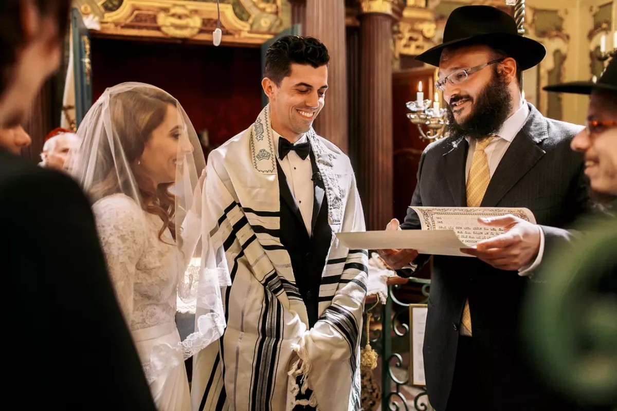 Frischvermähltes, lächelndes Paar zeigt die Ketuba, den jüdischen religiösen Ehevertrag, nach der Zeremonie unter der Chuppa.