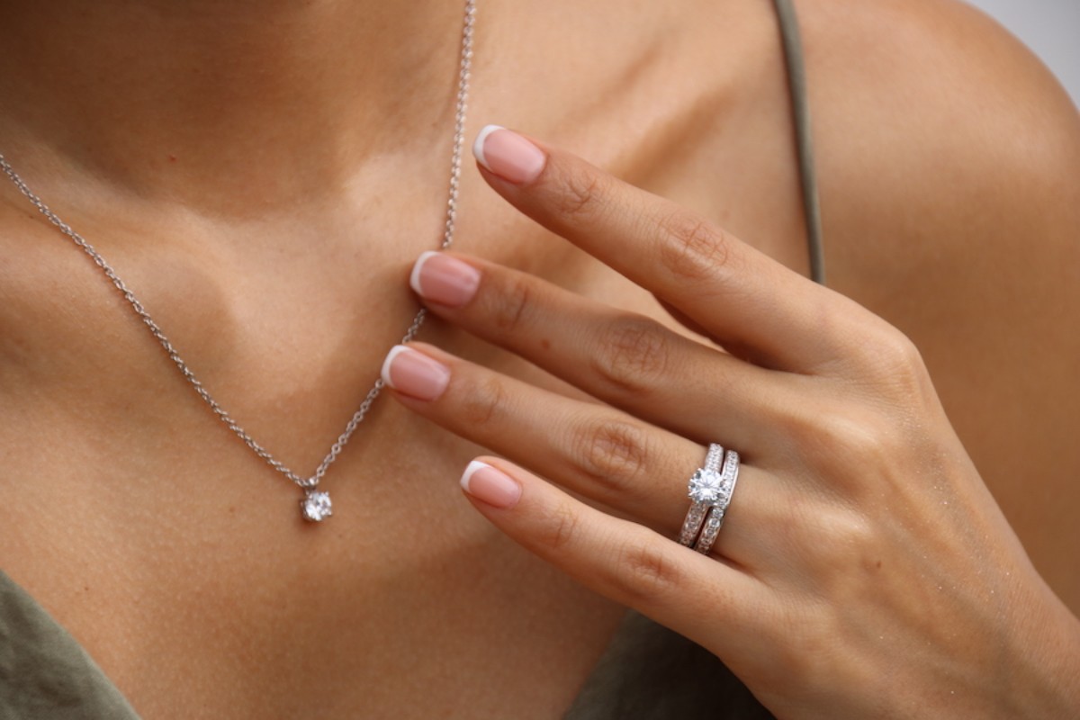 Gros plan sur une main portant un solitaire diamant avec alliances pavées en or blanc, accompagné d’un collier solitaire, illustrant l’éclat d’un serti griffe Celinni.