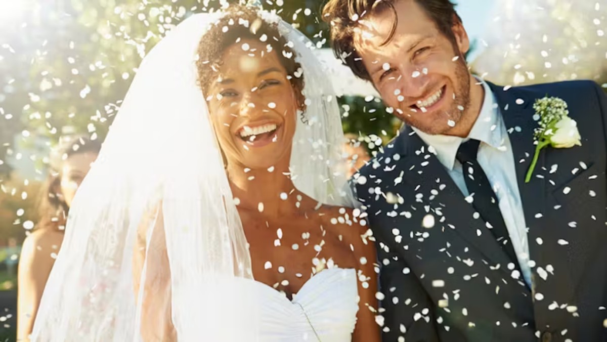 Jeune couple de mariés souriant sous une pluie de riz à la sortie de la cérémonie, symbole de prospérité et de bonheur selon la tradition de mariage européenne.