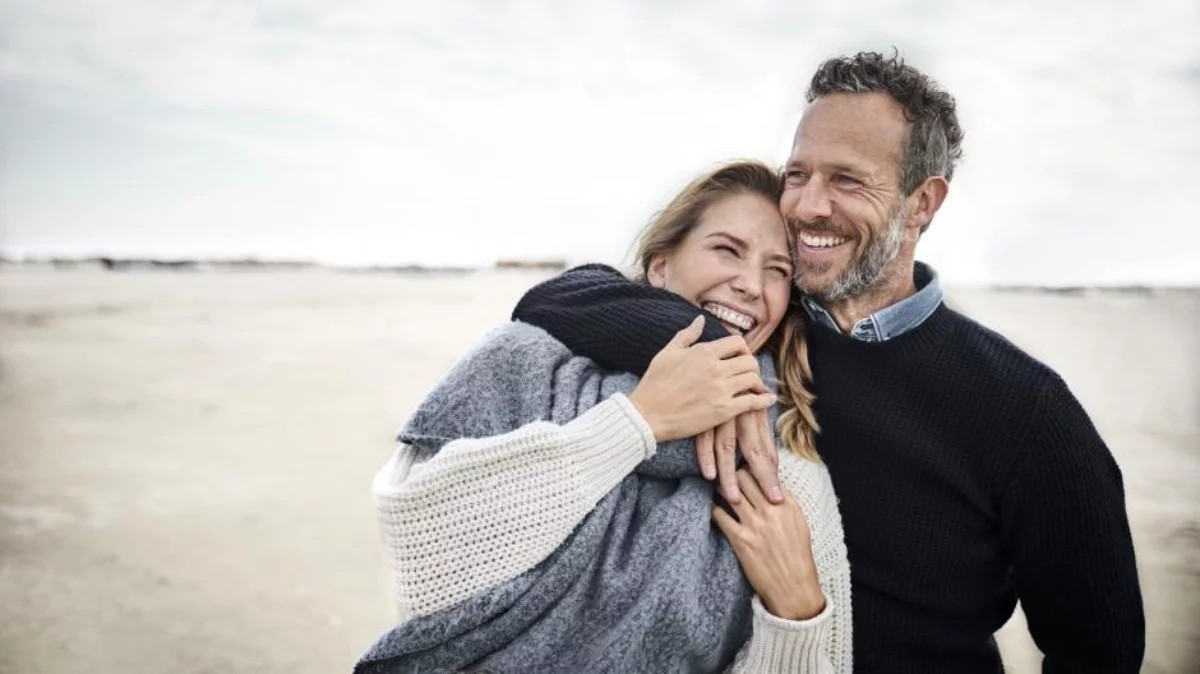 Ein vertrautes, lächelndes Paar, umarmt sich an einem Strand und feiert seinen 23. Hochzeitstag – die Beryllhochzeit